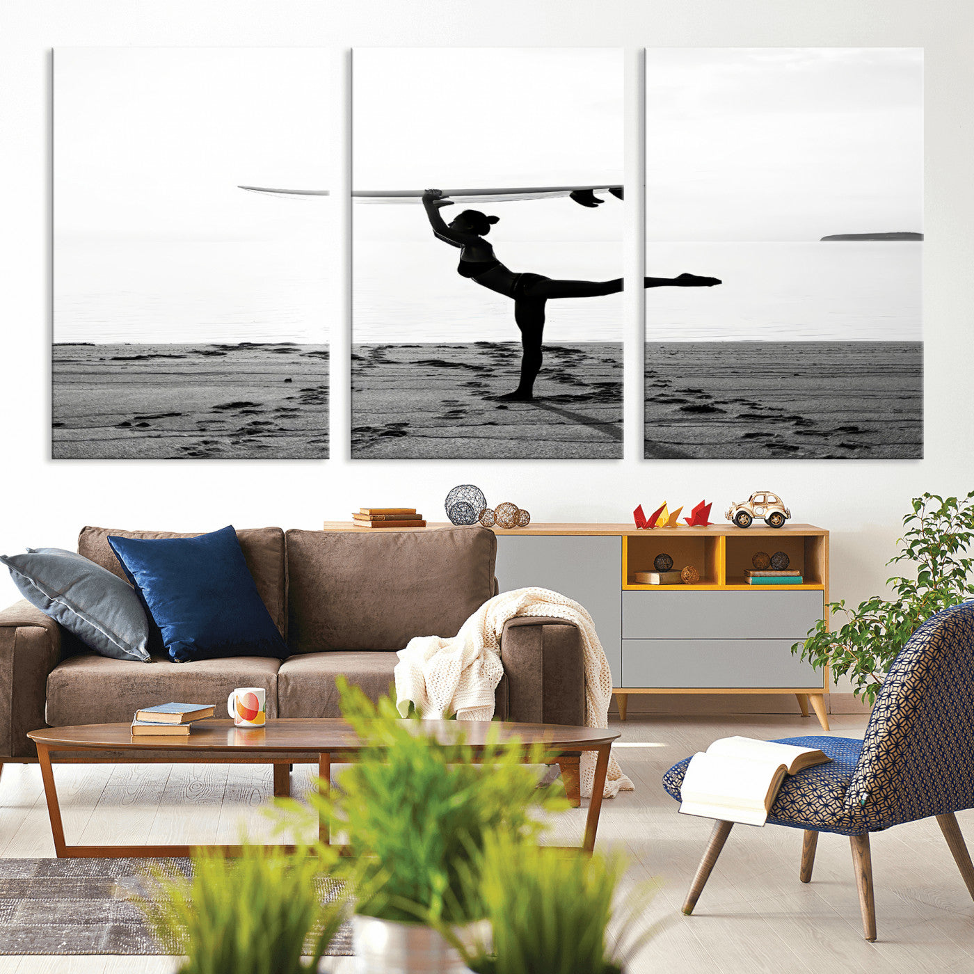 A woman balances a surfboard on her head while striking a yoga pose on the beach, silhouetted against a calm ocean horizon.