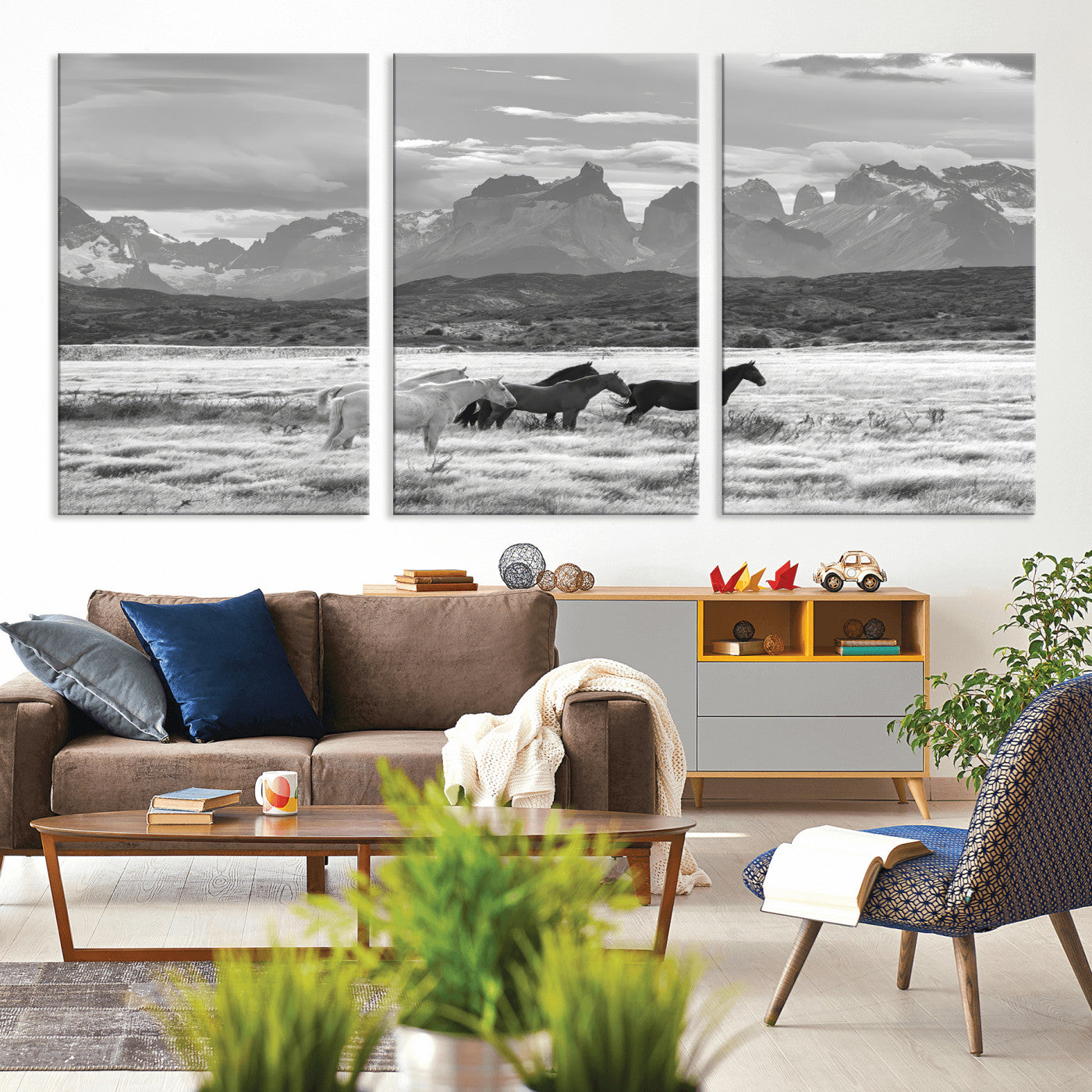 A black and white landscape of wild horses grazing in a vast grassland with towering mountains in the background, creating a moody and rustic western aesthetic.