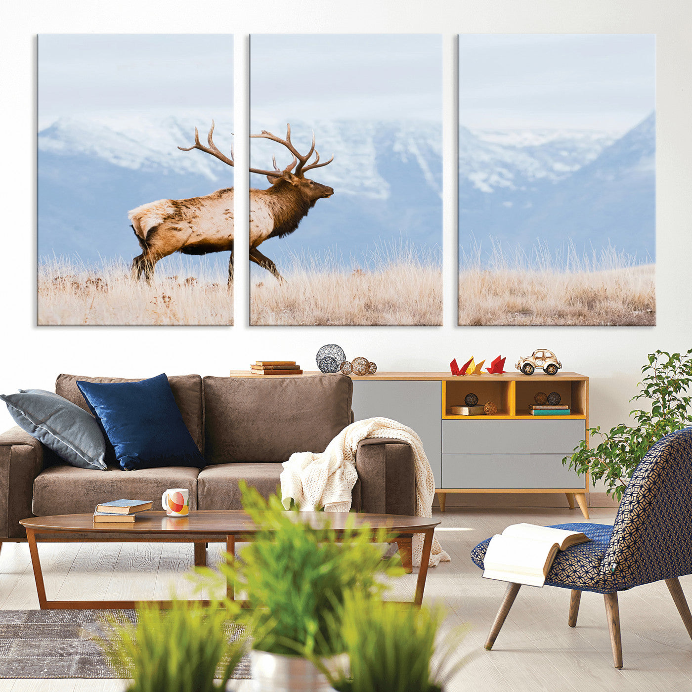 An elk walking on snowy grassland with majestic mountains in the background, ideal for rustic lodge or cabin wall decor.