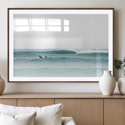 Minimalist photo of a lone surfer on calm aqua waves under bright sky, perfect for Scandinavian coastal or serene ocean-inspired home decor.