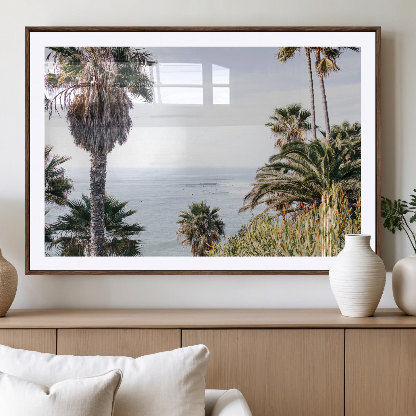 Scenic coastal view with tall palm trees overlooking a calm ocean, soft blue waves, and surfers in the distance, creating a peaceful tropical vibe.