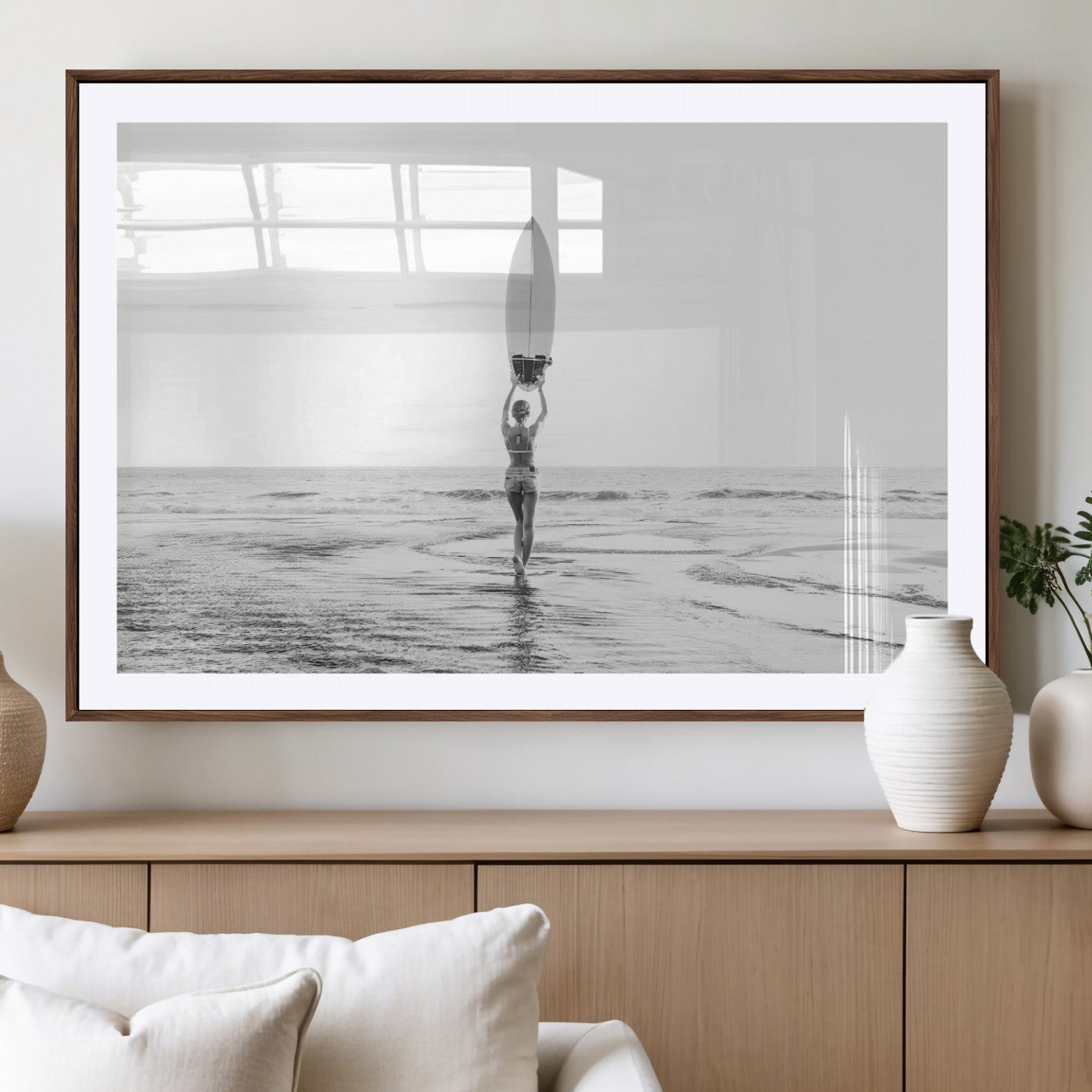 Black and white image of a female surfer holding a surfboard above her head while walking toward the ocean, creating a minimalist and bold coastal aesthetic.