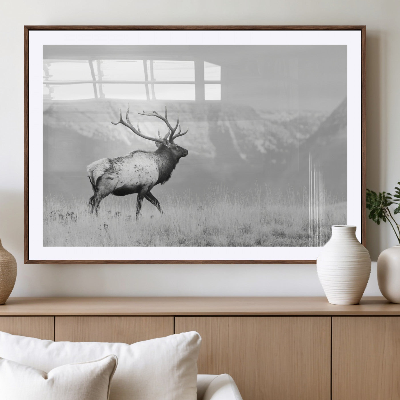 Black and white photograph of a majestic elk standing in a grassy field with snow-capped mountains in the background, creating a bold and rustic wilderness scene.