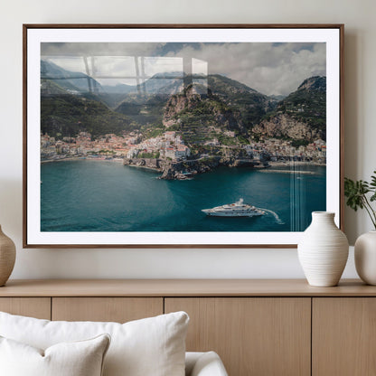 Aerial view of Amalfi Coast, Italy, with colorful hillside houses, lush green mountains, and a luxury yacht sailing in turquoise waters.