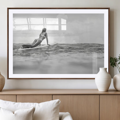 A black and white ocean scene featuring a surfer girl waiting on her board, gazing at the horizon, capturing a tranquil and adventurous coastal moment.