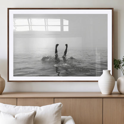 A black and white minimalist water scene capturing a playful splash as a swimmer dives upside down, creating a carefree and artistic aquatic aesthetic.