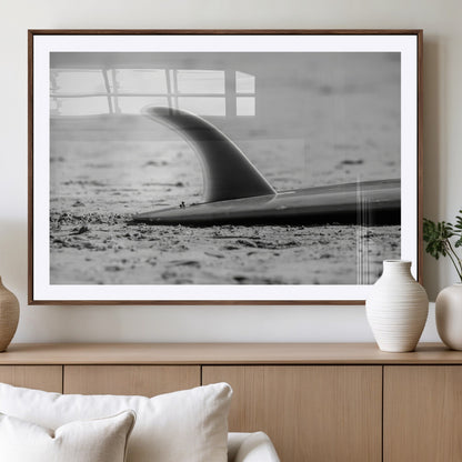 A black and white close-up of a surfboard fin resting on the sandy shore, highlighting minimalist beach aesthetics and classic surf culture.