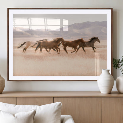 A herd of wild horses galloping through a sunlit desert plain with mountains in the background, perfect for rustic or western-themed wall decor.