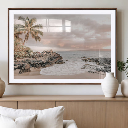 A peaceful beach scene with a palm tree and rocks, soft waves washing onto the shore under a soft pastel sky at sunset.
