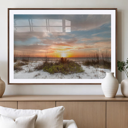 A tranquil beach scene featuring golden sunset hues over the water, with grasses in the foreground and a peaceful, serene atmosphere.