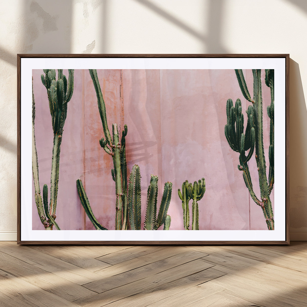 Framed canvas of tall green cacti against a soft pink wall, ideal for modern desert or colorful southwest-inspired home decor.