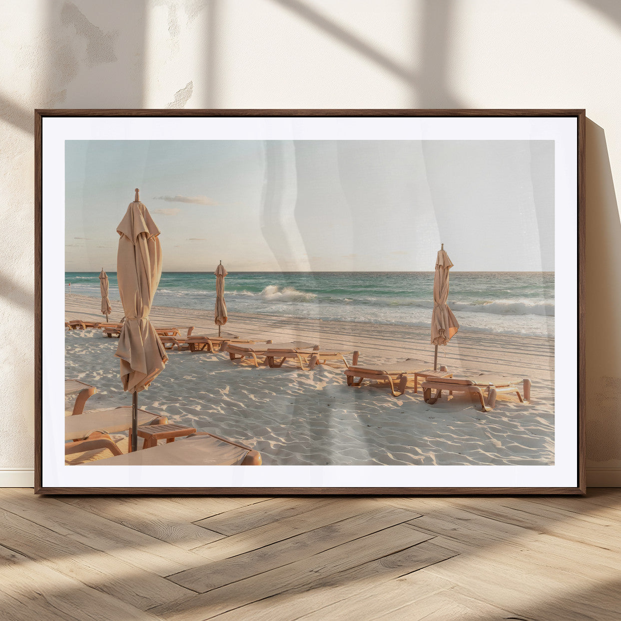 Minimalist photo of empty beach loungers and umbrellas on soft sand, ideal for calm seaside or pastel coastal-style home decor.