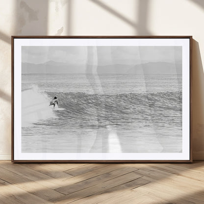Monochrome photo of a surfer riding a wave with distant mountains, ideal for coastal motion or black and white surf-themed wall decor.