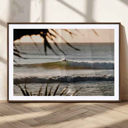 Photo of a surfer riding a golden hour wave at sunset, with tropical tones and dreamy light, perfect for tropical boho or coastal home decor.