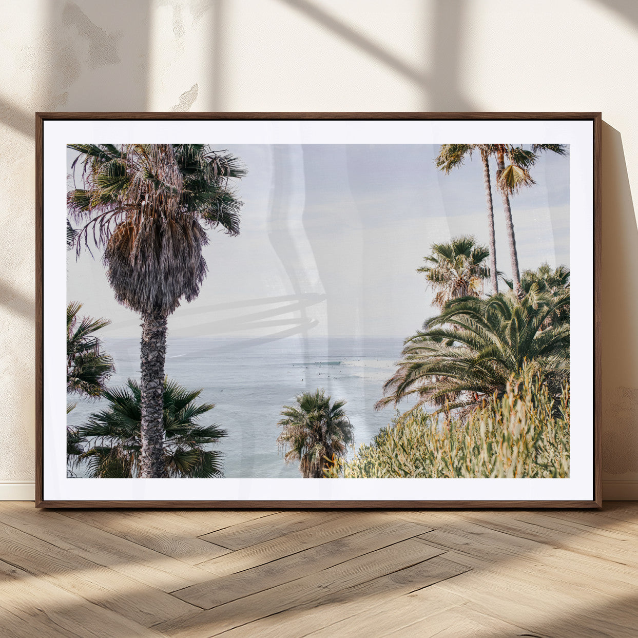 Scenic coastal view with tall palm trees overlooking a calm ocean, soft blue waves, and surfers in the distance, creating a peaceful tropical vibe.