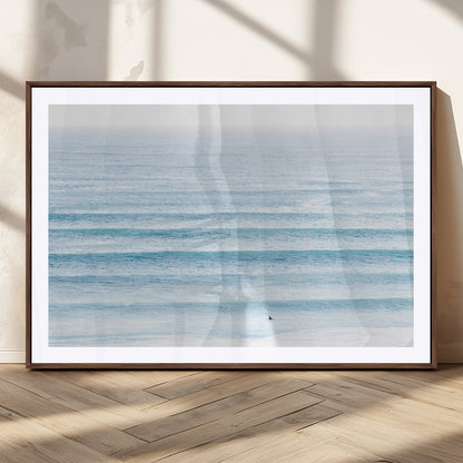 Minimalist ocean view with soft blue waves and a lone surfer, creating a serene and airy coastal aesthetic, perfect for tranquil home decor.