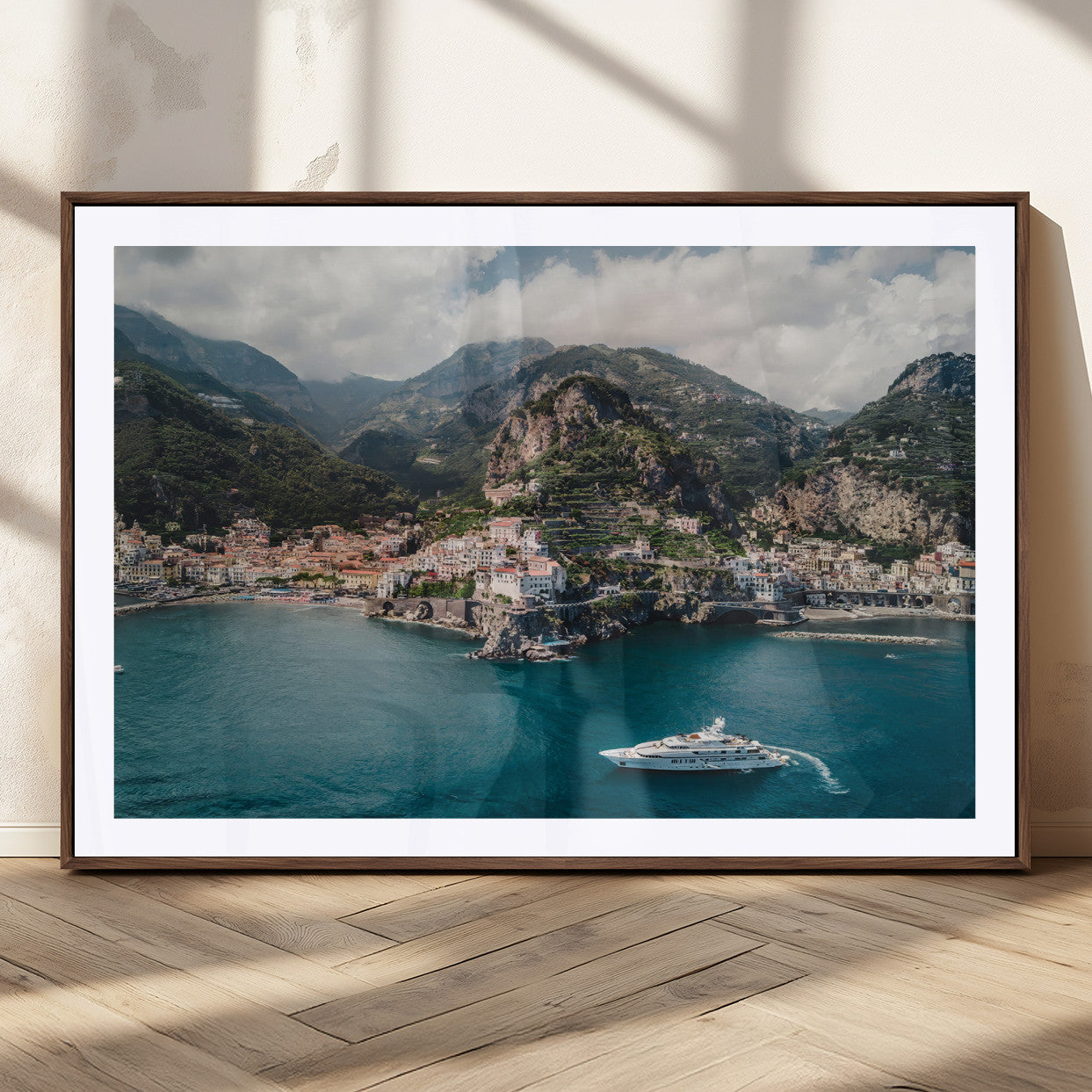 Aerial view of Amalfi Coast, Italy, with colorful hillside houses, lush green mountains, and a luxury yacht sailing in turquoise waters.