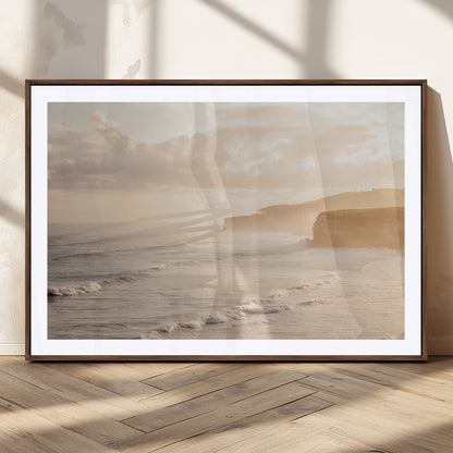 Golden hour seascape with misty cliffs and gentle waves rolling towards the shore, capturing a tranquil and warm coastal atmosphere.