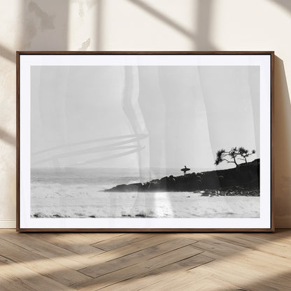Black and white photo of a surfer standing on rocky cliffs, gazing at the waves, embodying the spirit of adventure and solitude.