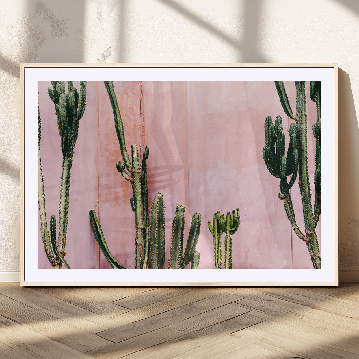 Framed canvas of tall green cacti against a soft pink wall, ideal for modern desert or colorful southwest-inspired home decor.