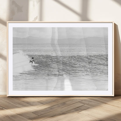 Monochrome photo of a surfer riding a wave with distant mountains, ideal for coastal motion or black and white surf-themed wall decor.