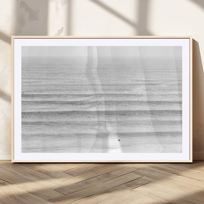 Monochrome photo of a lone surfer in calm layered waves, perfect for minimalist coastal or moody ocean-inspired wall decoration.
