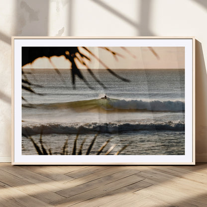 Photo of a surfer riding a golden hour wave at sunset, with tropical tones and dreamy light, perfect for tropical boho or coastal home decor.