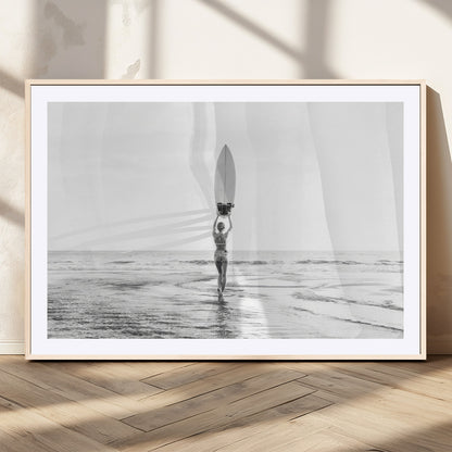 Black and white image of a female surfer holding a surfboard above her head while walking toward the ocean, creating a minimalist and bold coastal aesthetic.