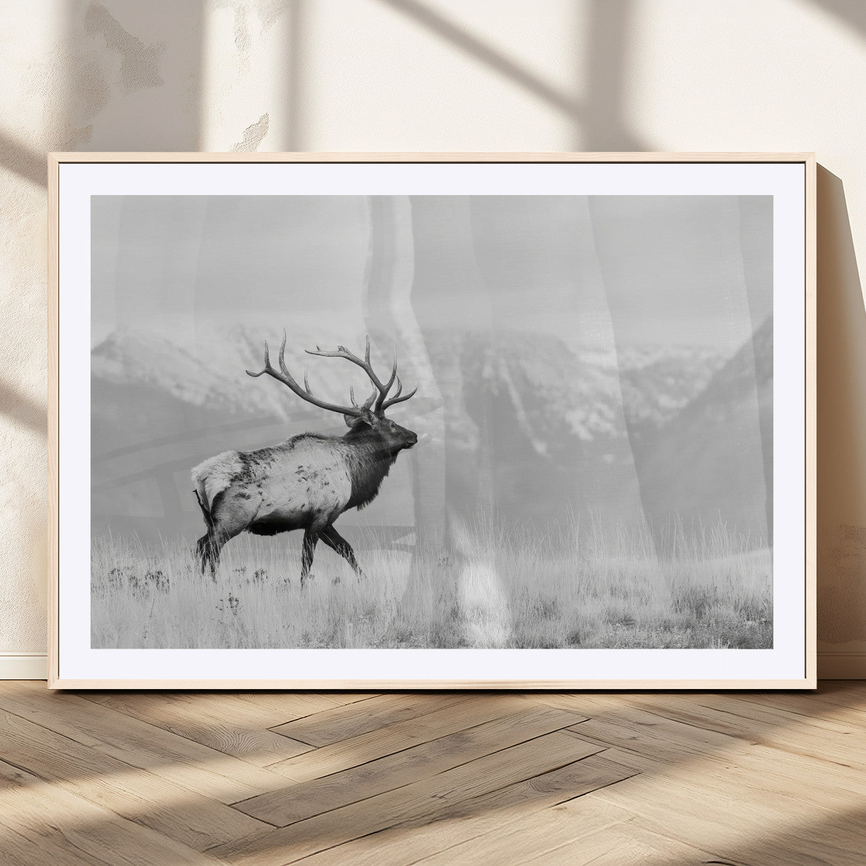Black and white photograph of a majestic elk standing in a grassy field with snow-capped mountains in the background, creating a bold and rustic wilderness scene.