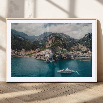 Aerial view of Amalfi Coast, Italy, with colorful hillside houses, lush green mountains, and a luxury yacht sailing in turquoise waters.