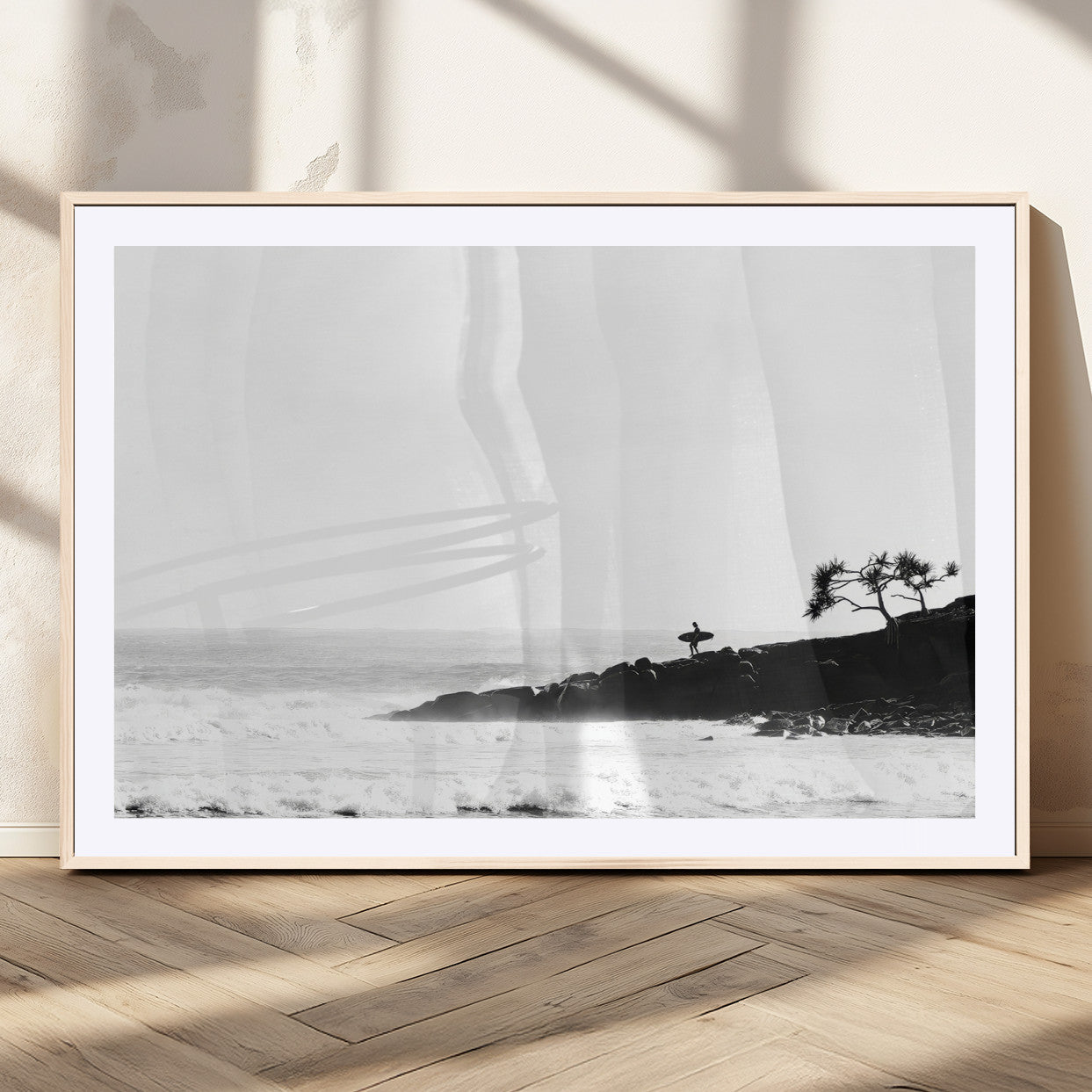 Black and white photo of a surfer standing on rocky cliffs, gazing at the waves, embodying the spirit of adventure and solitude.