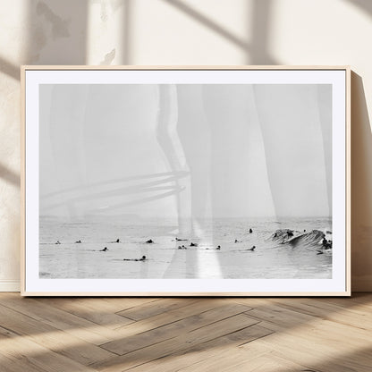 A group of surfers floating in the ocean, waiting for waves under a vast, moody sky, captured in black and white.