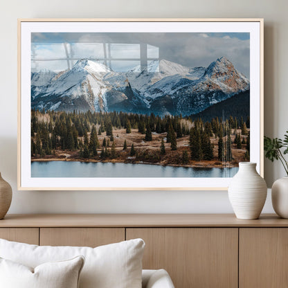 Framed canvas of snowy mountain peaks with pine forest and alpine lake, perfect for winter cabin or wilderness-inspired home decor.