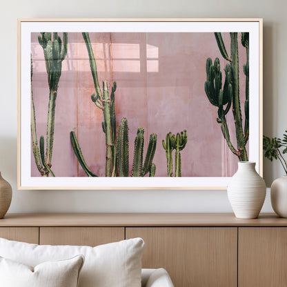 Framed canvas of tall green cacti against a soft pink wall, ideal for modern desert or colorful southwest-inspired home decor.