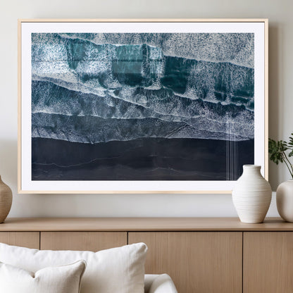 Canvas of aerial ocean waves crashing onto a black sand beach in moody tones, ideal for modern coastal or minimalist home decor.