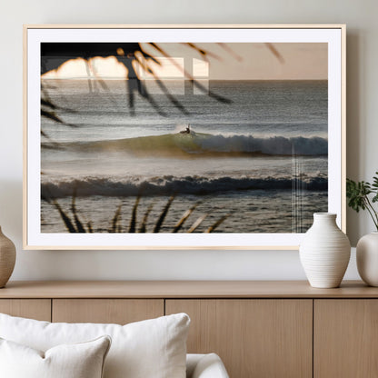 Photo of a surfer riding a golden hour wave at sunset, with tropical tones and dreamy light, perfect for tropical boho or coastal home decor.