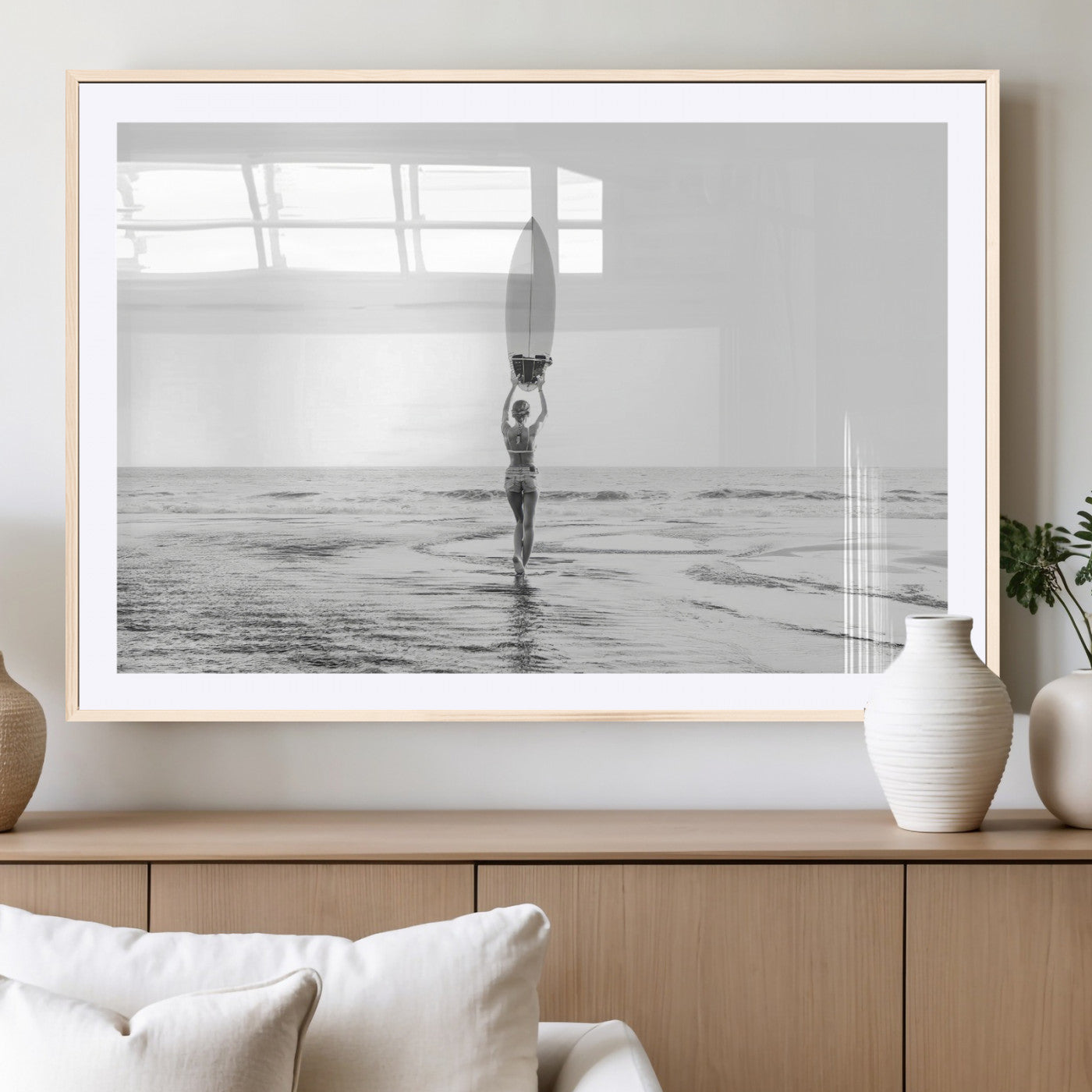 Black and white image of a female surfer holding a surfboard above her head while walking toward the ocean, creating a minimalist and bold coastal aesthetic.
