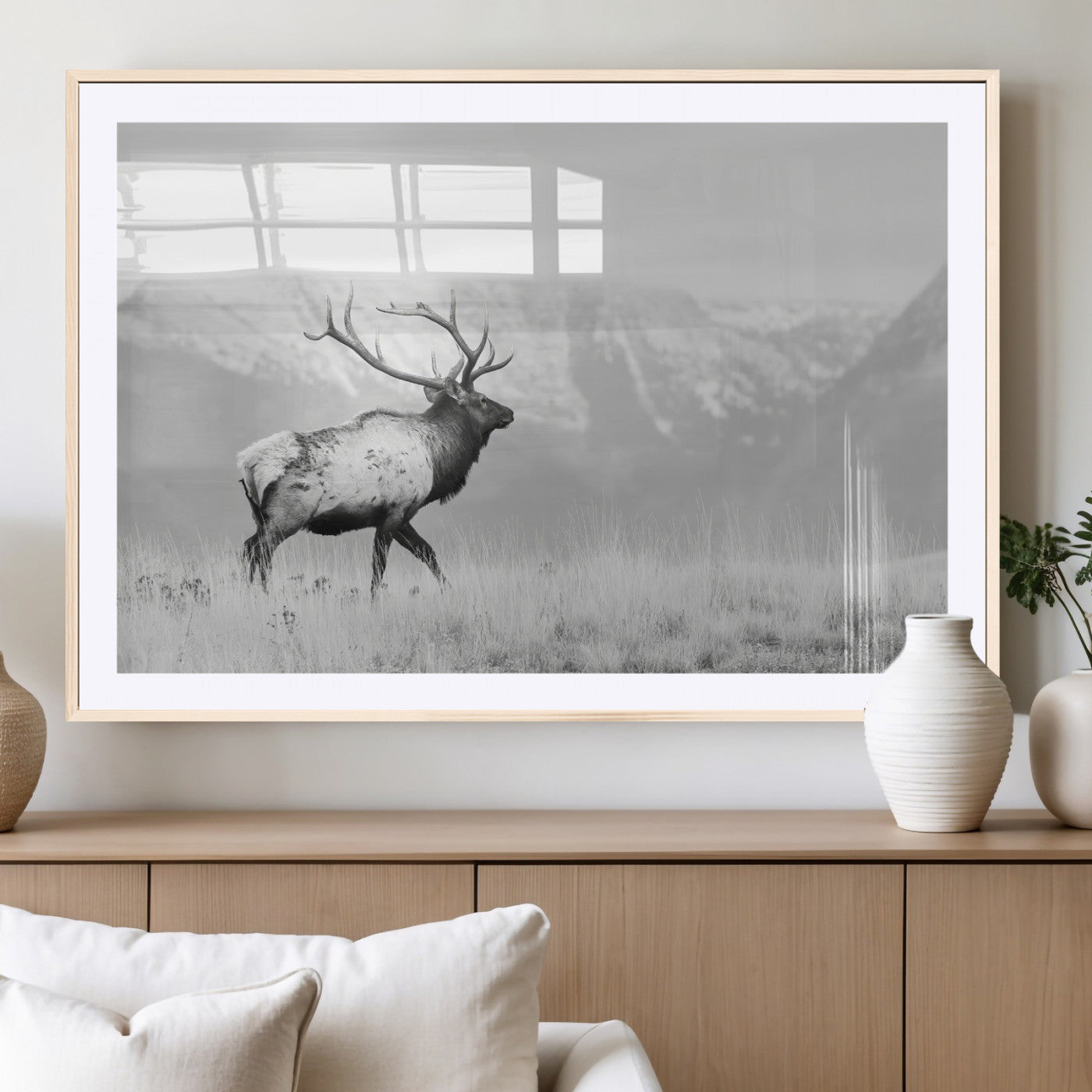 Black and white photograph of a majestic elk standing in a grassy field with snow-capped mountains in the background, creating a bold and rustic wilderness scene.