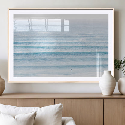 Minimalist ocean view with soft blue waves and a lone surfer, creating a serene and airy coastal aesthetic, perfect for tranquil home decor.