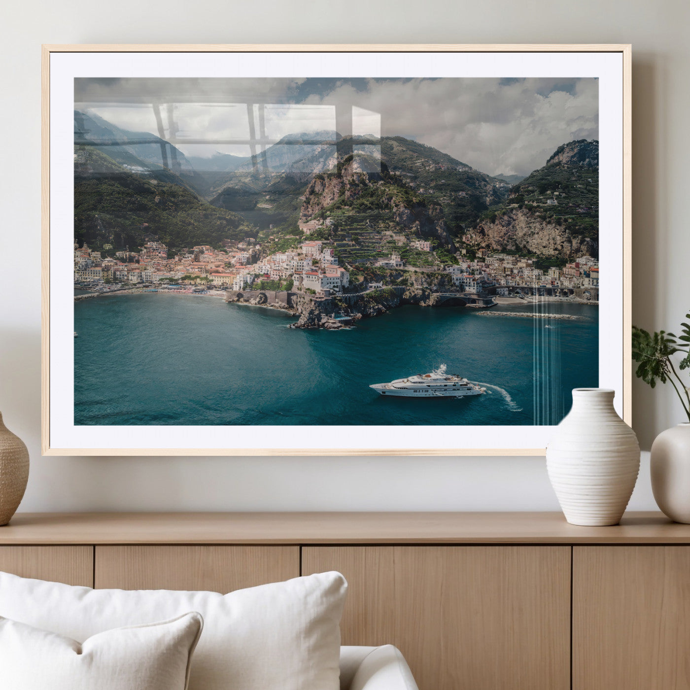 Aerial view of Amalfi Coast, Italy, with colorful hillside houses, lush green mountains, and a luxury yacht sailing in turquoise waters.