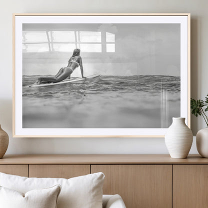 A black and white ocean scene featuring a surfer girl waiting on her board, gazing at the horizon, capturing a tranquil and adventurous coastal moment.