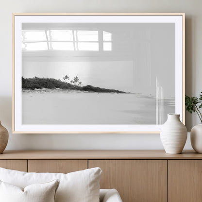A black and white minimalist coastal scene with a vast open beach, distant palm trees, and a lone figure walking along the shoreline, evoking serenity and solitude.