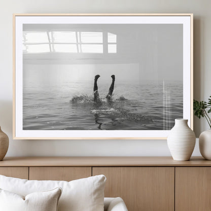 A black and white minimalist water scene capturing a playful splash as a swimmer dives upside down, creating a carefree and artistic aquatic aesthetic.