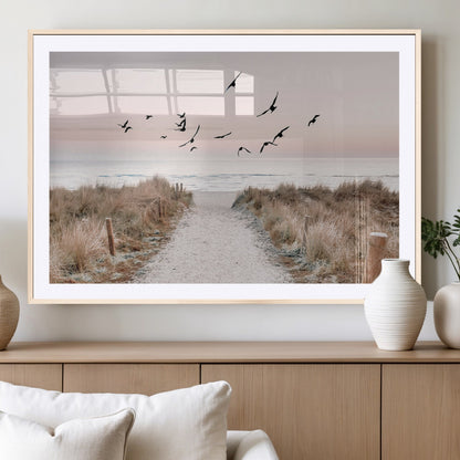 A peaceful coastal pathway leading to the ocean, with birds flying across a soft pastel sky, creating a calm and scenic beach atmosphere.