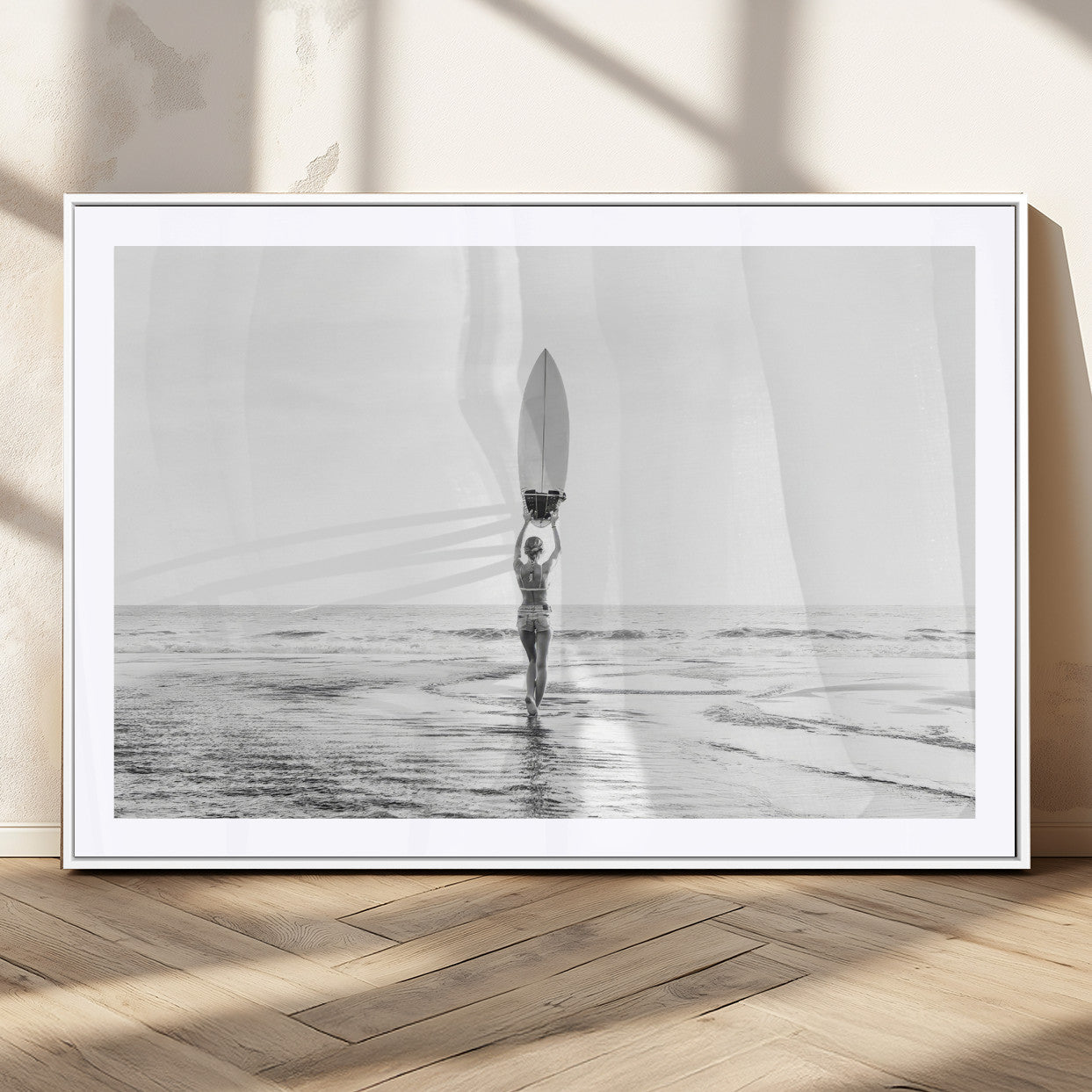 Black and white image of a female surfer holding a surfboard above her head while walking toward the ocean, creating a minimalist and bold coastal aesthetic.