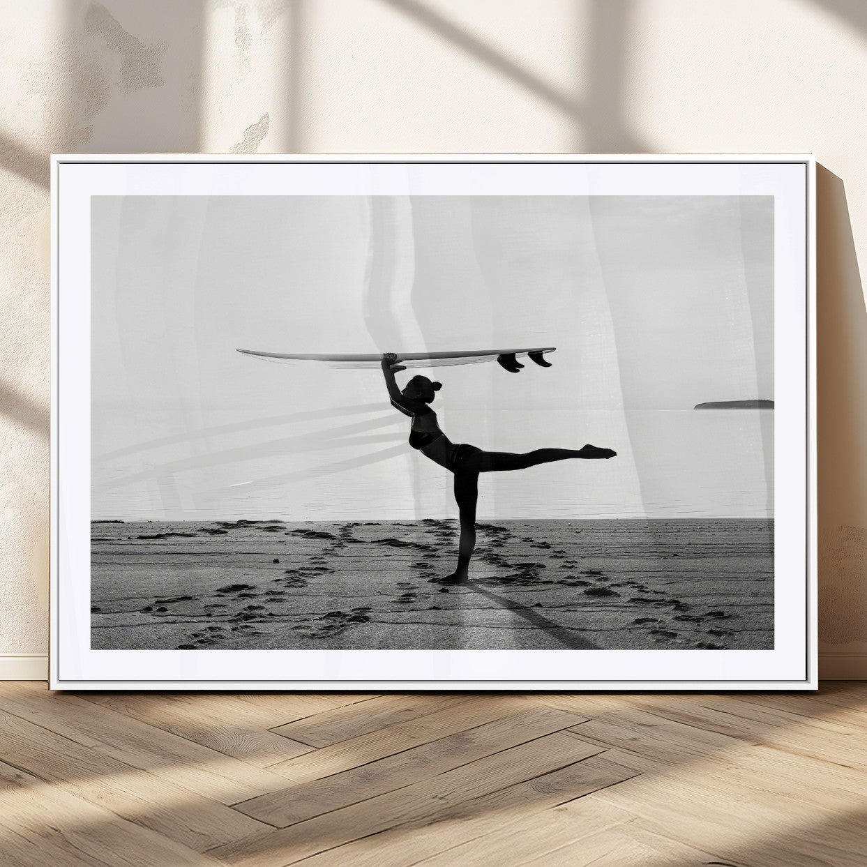 A woman balances a surfboard on her head while striking a yoga pose on the beach, silhouetted against a calm ocean horizon.