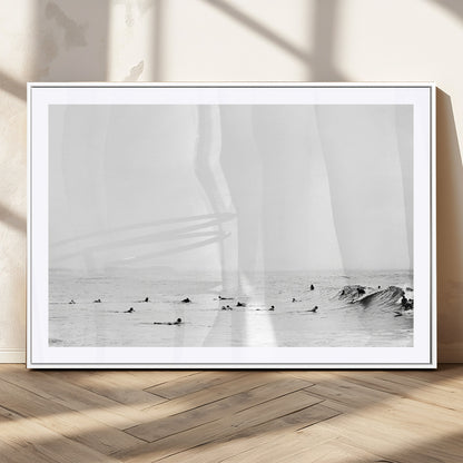 A group of surfers floating in the ocean, waiting for waves under a vast, moody sky, captured in black and white.
