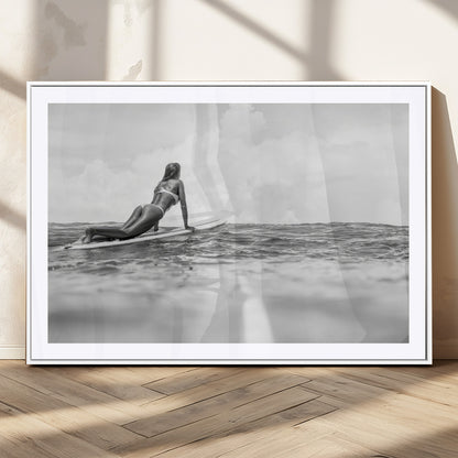 A black and white ocean scene featuring a surfer girl waiting on her board, gazing at the horizon, capturing a tranquil and adventurous coastal moment.