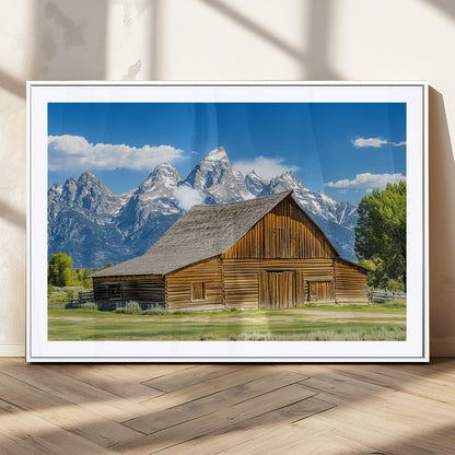 A rustic wooden barn sits in front of towering mountain peaks under a clear blue sky, perfect for farmhouse or cabin style interiors.