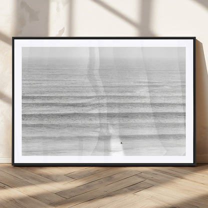 Monochrome photo of a lone surfer in calm layered waves, perfect for minimalist coastal or moody ocean-inspired wall decoration.